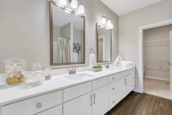 Elegantly designed bathroom featuring dual sinks with sleek faucets, ample white cabinetry, and decorative glass jars for a luxurious touch.