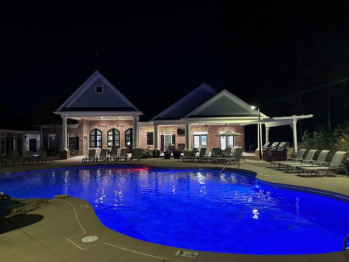 Elegant nighttime view of a luxurious apartment complex with a beautifully illuminated pool and relaxing lounge chairs.