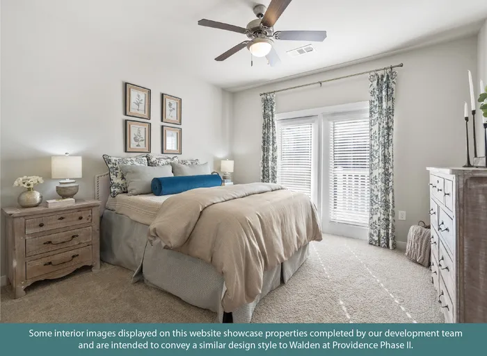 Elegant bedroom with cozy bedding, stylish wall art, and abundant natural light from double windows with patterned curtains, creating a serene and inviting atmosphere.