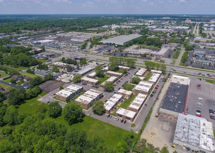 Aerial view of a vibrant suburban neighborhood with modern apartment complexes surrounded by lush greenery, showcasing convenient access to nearby amenities and ample parking space.