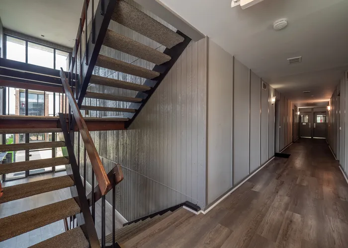 Modern apartment staircase with sleek wooden railings and contemporary design, leading to a well-lit hallway with elegant flooring and stylish paneling.