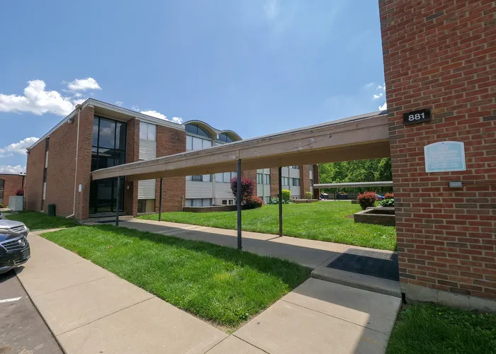 Charming brick apartment building with modern windows, surrounded by lush green lawns and a welcoming pathway under a clear blue sky.