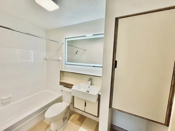 Bright and modern bathroom featuring a sleek bathtub, stylish sink, and ample storage with a contemporary mirror.