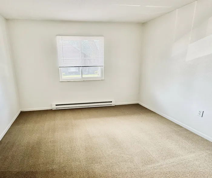 Bright, inviting bedroom with natural light, neutral walls, and cozy carpeting perfect for a relaxing retreat.