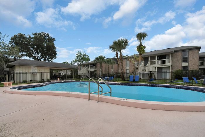 Inviting apartment complex featuring a sparkling outdoor pool surrounded by lush palm trees and modern lounge chairs.