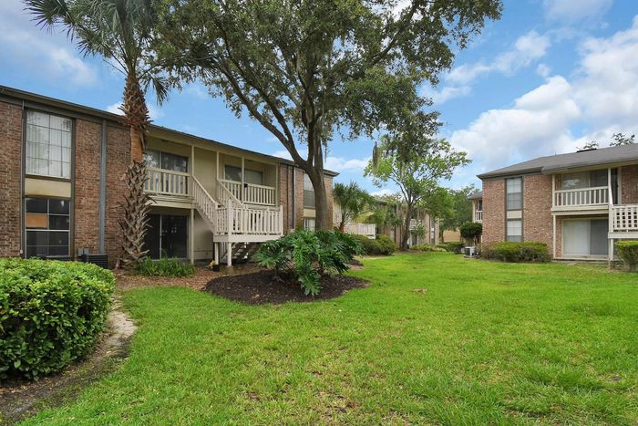 Charming apartment complex with lush green landscaping, featuring spacious balconies and elegant brick facade.