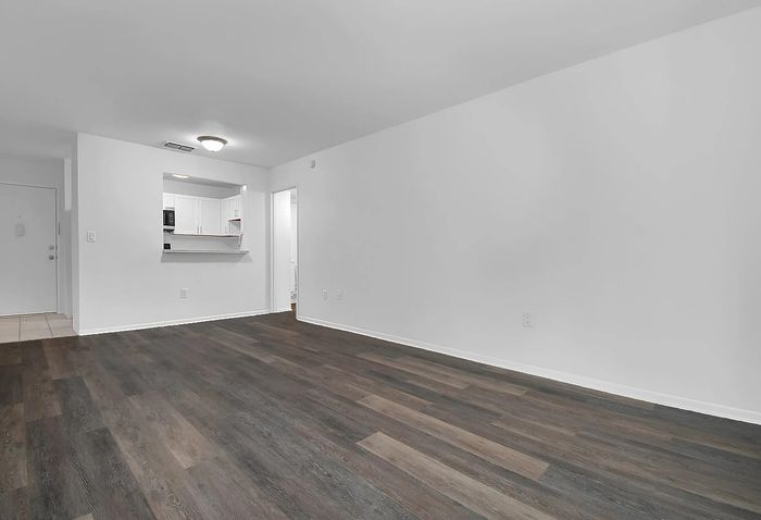 Spacious living area with elegant wooden flooring and bright, open-concept layout leading to a modern kitchen.