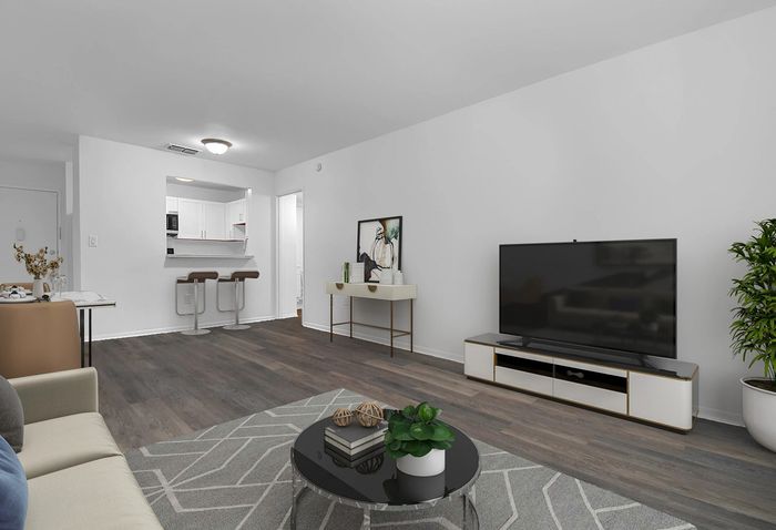 Modern open-concept living room with sleek furniture, warm wood flooring, and a cozy kitchen area in the background.