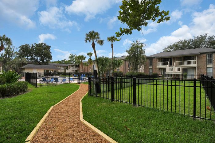Charming apartment complex featuring a vibrant green lawn, palm trees, and a relaxing pool area under a bright blue sky.