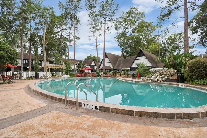 Charming apartment complex with a crystal-clear swimming pool surrounded by lush greenery and cozy A-frame houses, offering a serene and inviting atmosphere.