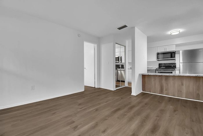 Modern open-concept apartment showcasing sleek hardwood floors, a bright kitchen with granite countertops, and stainless steel appliances.