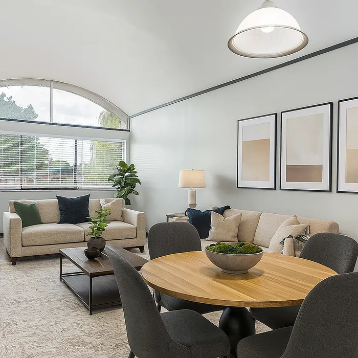 Inviting living room with modern decor, featuring cozy beige sofas, elegant framed artwork, and a stylish round dining table overlooking a large window.