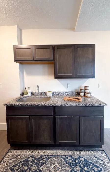 Modern kitchen area with sleek dark wood cabinets, granite countertop, and stylish decor.