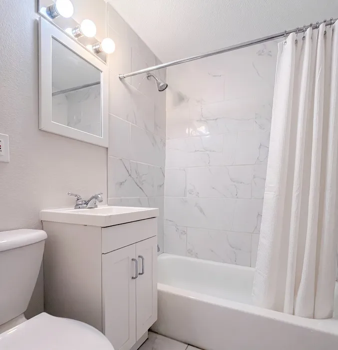 Bright and modern bathroom featuring elegant marble tiles, sleek vanity, and a cozy bathtub with a fresh white curtain.