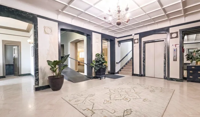 Elegant apartment lobby featuring a stylish chandelier, decorative marble accents, and lush potted plants, offering a welcoming and sophisticated entryway.