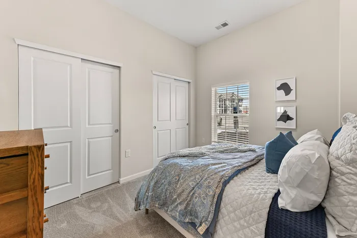 Bright and cozy bedroom featuring soft beige walls, a plush bed with elegant linens, sliding closet doors, and a window with scenic outdoor views.