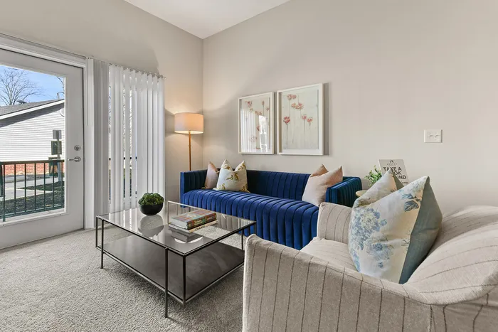 Chic living room featuring a plush blue sofa, elegant decor, and a bright ambiance with modern glass door leading to outdoor views.