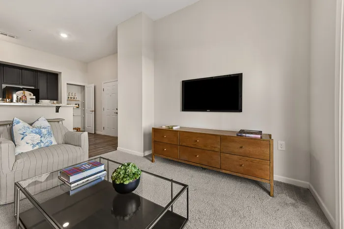 Modern living room with elegant decor, featuring a cozy armchair, sleek TV, and stylish wooden furniture against a neutral backdrop.