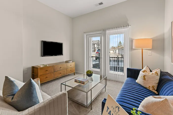 Chic living room featuring a sleek glass coffee table, stylish navy-blue sofa, and large window providing ample natural light.