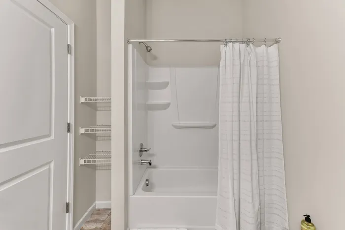 Modern bathroom featuring a sleek white bathtub with an elegant shower curtain, convenient shelving, and stylish neutral tones.