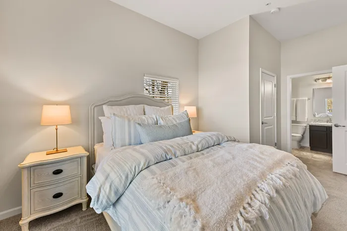 Elegant bedroom with plush bedding, soft lighting from table lamps, and a view into an en-suite bathroom.