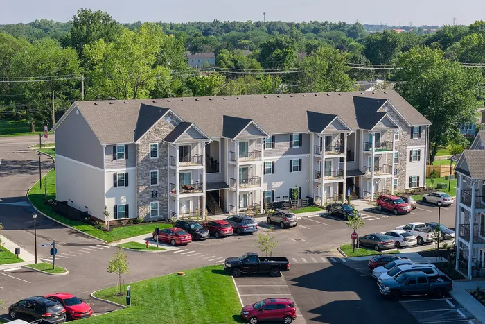 Modern three-story apartment complex with spacious balconies and ample parking, surrounded by lush greenery.
