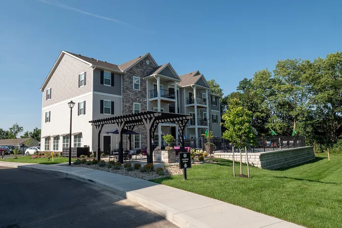 Charming three-story apartment building with stone accents and a welcoming pergola entrance, surrounded by lush green landscaping.