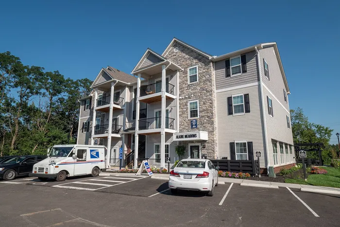 Charming three-story apartment building with stone accents, inviting balconies, and ample parking space on a sunny day.
