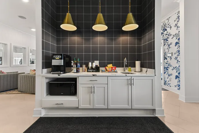 Chic apartment kitchenette with modern white cabinetry, elegant pendant lighting, and a convenient coffee station.