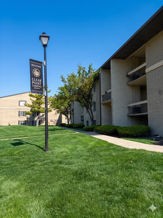 Serene Clear Point Gardens apartment community with lush green lawns and traditional architecture under a clear blue sky.
