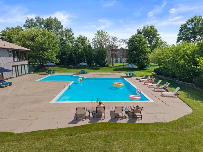 Inviting outdoor pool area surrounded by lush greenery, featuring lounge chairs and vibrant inflatables under the clear blue sky.