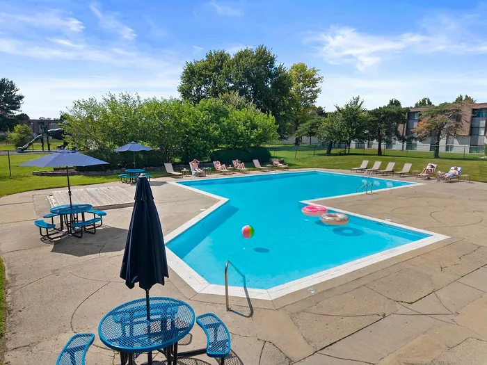 Inviting outdoor pool area with sun loungers, colorful floats, and shaded picnic tables for a relaxing day under the blue sky.