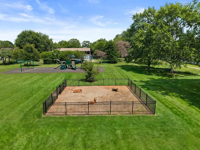 Charming outdoor space featuring a fenced dog park, lush green lawns, and a modern playground under a clear blue sky.