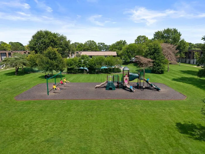 Spacious playground surrounded by lush greenery, featuring swings and slides, ideal for family fun and outdoor enjoyment.