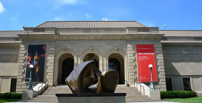 Elegant museum facade with grand entrance, showcasing a modern sculpture and vibrant banners on a sunny day.