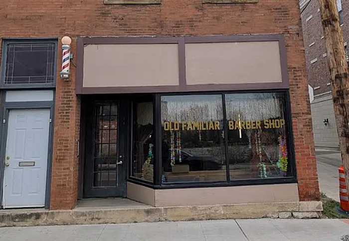 Charming brick storefront of Old Familiar Barber Shop with large display windows and traditional barber pole, inviting and nostalgic.