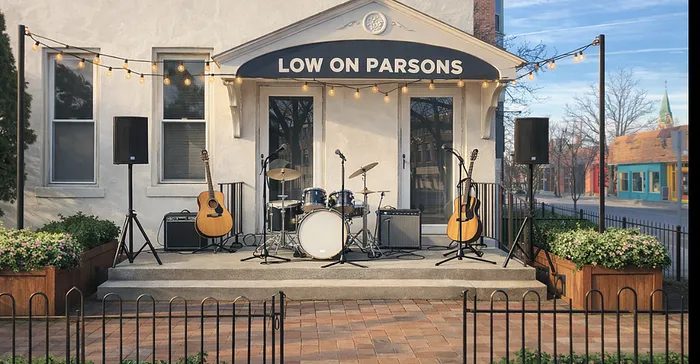Charming outdoor music stage at 'Low on Parsons' featuring acoustic guitars, a drum set, speakers, and string lights for a vibrant street performance ambiance.