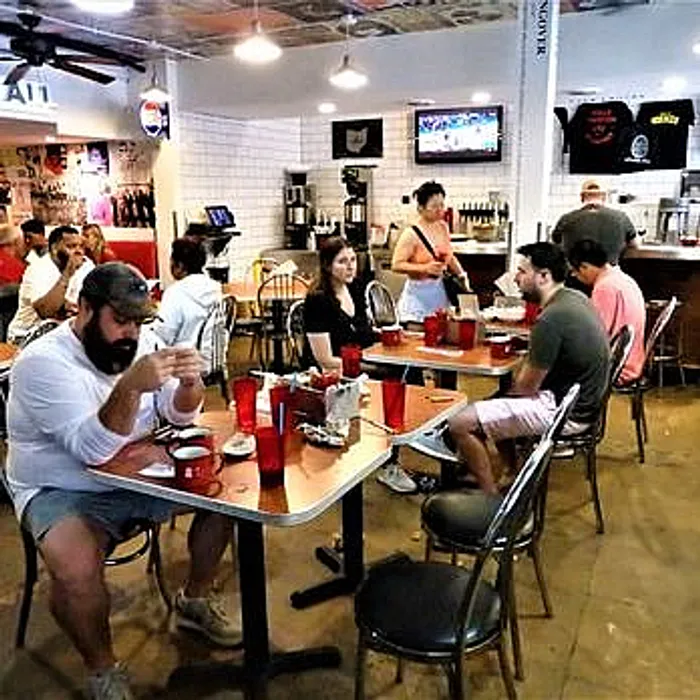 Cozy and vibrant cafe interior with people enjoying meals at stylish wooden tables; warm ambiance enhanced by eclectic decor and inviting atmosphere.
