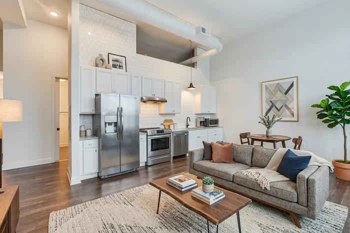 Modern open-concept apartment with sleek kitchen, cozy living area, and stylish decor featuring neutral tones and vibrant plant accents.