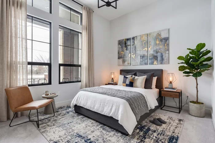 Bright and elegant bedroom with large windows, featuring stylish decor, a cozy bed, and a lush indoor plant for a serene ambiance.