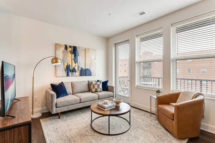 Bright and inviting living room with modern decor, featuring a cozy gray sofa, chic wall art, and large windows offering ample natural light.