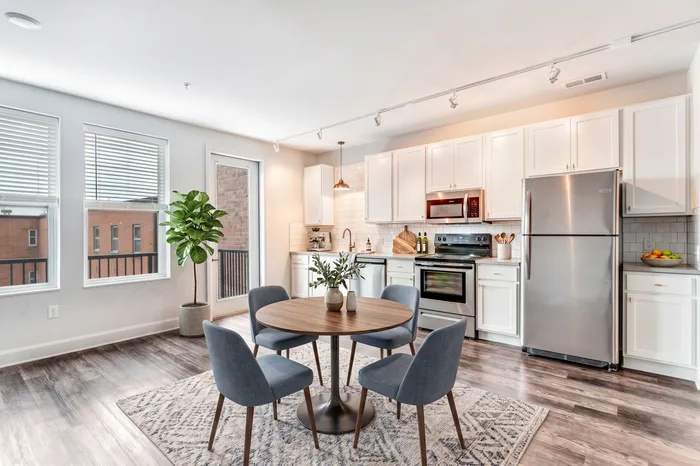 Bright and modern open-plan kitchen and dining area with sleek stainless steel appliances, elegant cabinetry, and a cozy round table for four.
