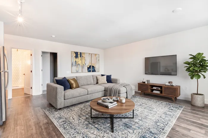 Modern living room with elegant grey sectional sofa, stylish wooden coffee table, and chic decor; bright and spacious with a large wall-mounted TV and vibrant artwork.