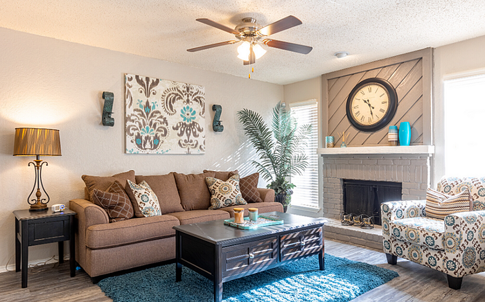 A2 floor plan inviting living room featuring a comfortable brown sofa, decorative pillows, stylish coffee table, and a charming fireplace with a large clock.