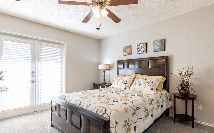 A2 floor plan bedroom with a wooden bed, floral bedding, and natural light through French doors.