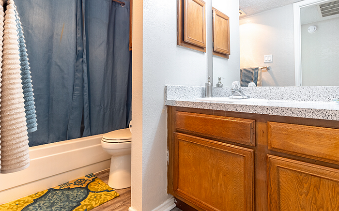 A2 floor plan bathroom with wooden cabinets, and a cozy shower space accented by a blue curtain.