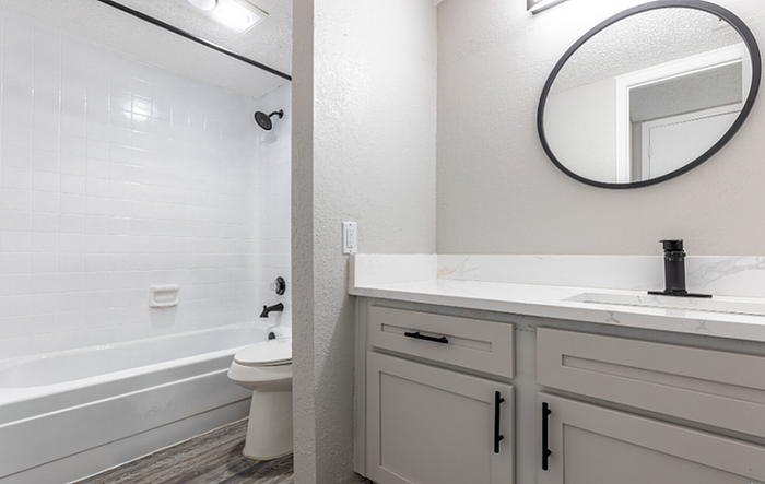 B1 Floor plan Designer bright contemporary bathroom with a sleek round mirror, white vanity, and modern fixtures.