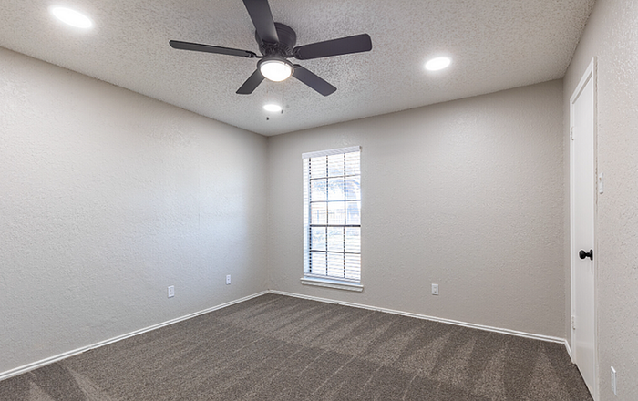 B1 Floor plan Guest bedroom with soft carpeting, a ceiling fan, and a bright window letting in natural light.