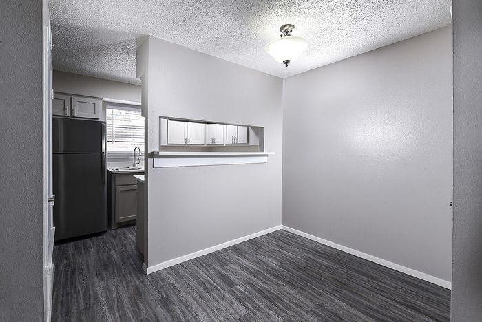 Bright dining area with modern lighting next to a sleek kitchen featuring dark wood flooring.