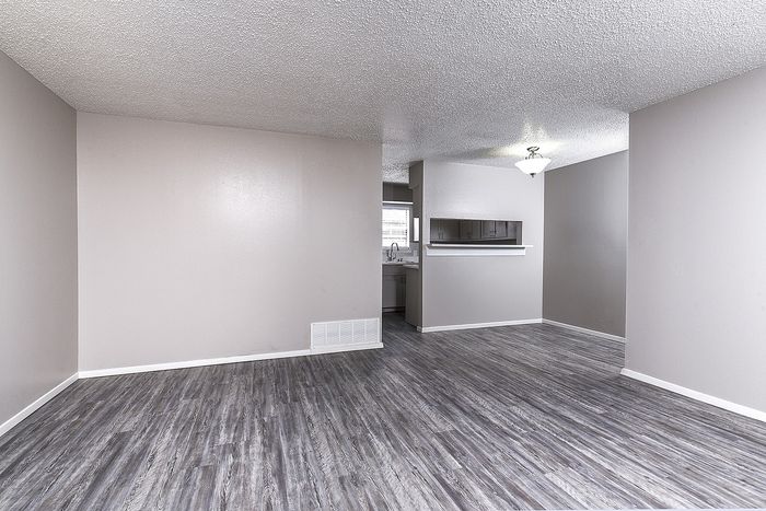 Bright living space with modern gray flooring and a view into the kitchen area.